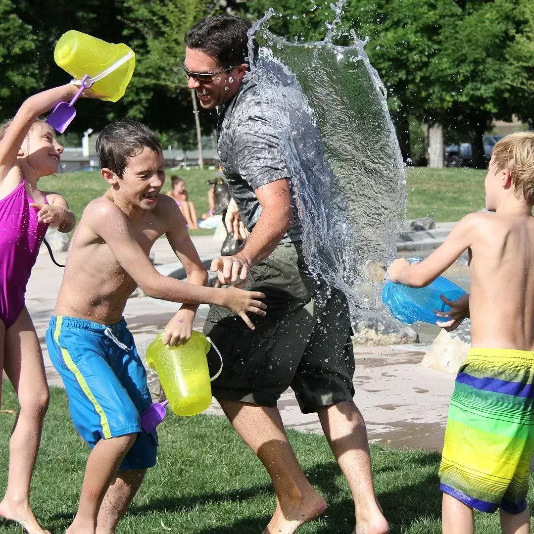 Kids playing with their father and throwing water from buckets on him